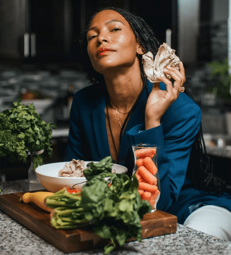 Chef Foxy holding an oyster mushroom beside a counter of fresh vegetables and herbs